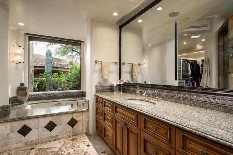 Wood cabinetry, a stone vanity and a window overlooking desert plantings.