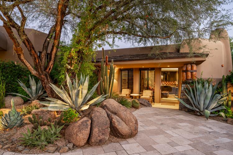 A sheltered entry framed by desert trees, agaves and natural boulders.
